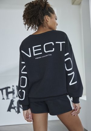 Black sweatshirt with white text, oversized fit, dropped shoulders, and matching black shorts. Features “FRENCH CONNECTION” logo prominently.