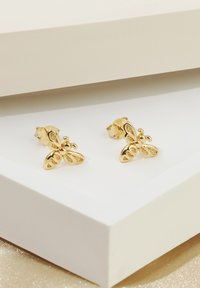 Guldörhängen i form av fjärilar med detaljerade urtag, med en polerad yta och säkerhetsstift, visade mot en vit bakgrund.