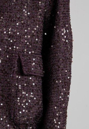 Tela adornada con lentejuelas en color púrpura oscuro, con una superficie texturizada y un pequeño bolsillo en el lado izquierdo.