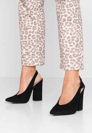 Czarne szpilki na obcasie typu slingback z zamszu, z zaostrzonym czubkiem i wyciętym wzorem. Charakteryzują się masywnym obcasem i klamrą przy kostce.