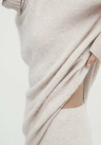 Ljusbeige tröja gjord av mjukt, fluffigt material med en ribbad halsringning. Designen har en lös passform och en exponerad sid söm.