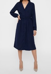 Abito blu navy a maniche lunghe con colletto, chiusura a bottoni sul davanti e cintura in vita. Presenta una gonna alla lunghezza del ginocchio e un tessuto leggermente testurizzato.
