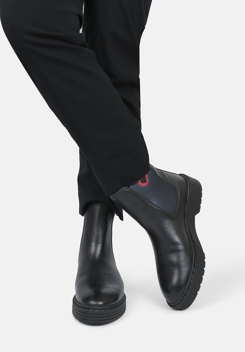 Bottines Chelsea noires en cuir avec une finition lisse, bout arrondi, panneaux latéraux élastiques et semelles robustes. Design minimaliste, sans quincaillerie visible.