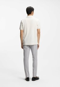 Vaaleabeige lyhythihainen poolopaita, jossa on klassinen kaulus, yhdistetty vaaleanharmaisiin räätälöityihin housuihin ja mustiin loafer-kenkiin.