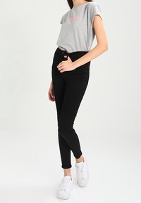 Camiseta gris de manga corta con texto rosa, combinada con jeans ajustados negros de cintura alta y zapatillas blancas. Diseño simple, look casual.