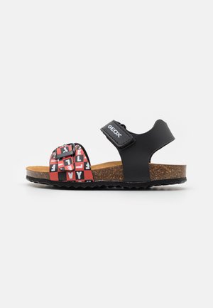 Sandalias negras con correa ajustable, plantilla de corcho, parte superior de patrón vibrante en rojo y negro con letras, suela de goma texturizada.