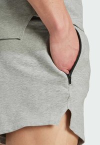 Jupe en mélange de coton gris clair avec une poche zippée sur le côté, un ourlet légèrement arrondi et des détails de couture visibles.