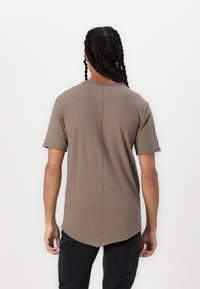 Braunes, kurzärmliges T-Shirt mit Rundhalsausschnitt und abgerundetem Saum, mit rohen Kanten und entspannter Passform, kombiniert mit schwarzen Cargo-Hosen.