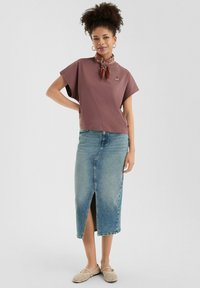 T-shirt en mauve doux avec des manches courtes et un d�étail de boutons, associé à une jupe en jean avec une fente à l'avant et une teinte bleu clair.