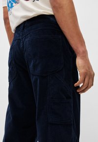 Pantaloni cargo din velur navy cu nervuri verticale, buzunare laterale și o croială ușor conică, prezentați din spate.