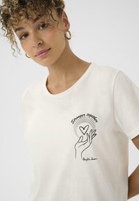 T-shirt en coton blanc avec un design dessiné à la main représentant une main tenant un cœur, accompagné du texte "Plus forts ensemble" en noir. Manches courtes.