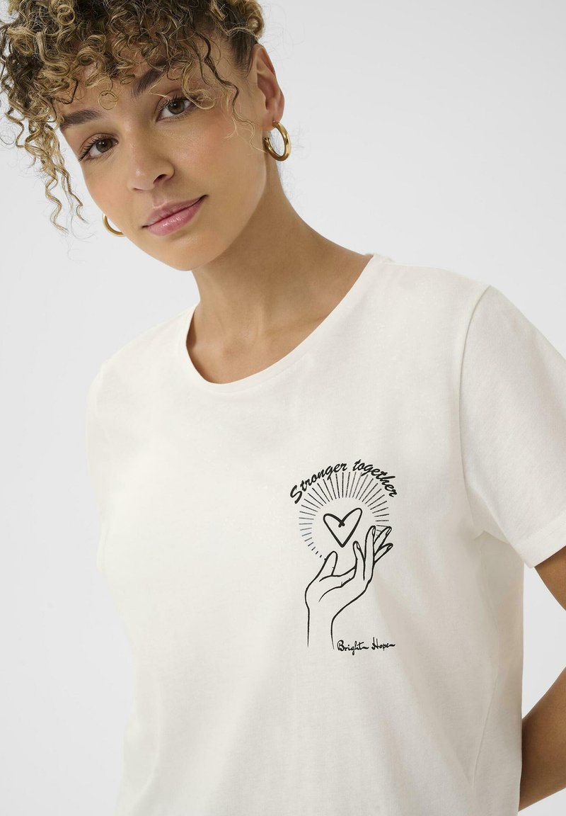 T-shirt en coton blanc avec un design dessiné à la main représentant une main tenant un cœur, accompagné du texte "Plus forts ensemble" en noir. Manches courtes.