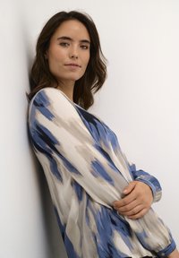 Locker sitzende Bluse aus leichtem Stoff mit einem blauen und beigen abstrakten Muster. Lange Ärmel mit Knopfdetails an den Bündchen.