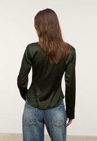 Blusa di raso verde scuro con una forma aderente e maniche lunghe, abbinata a jeans di denim blu chiaro con ricami a forma di stella sulle tasche.