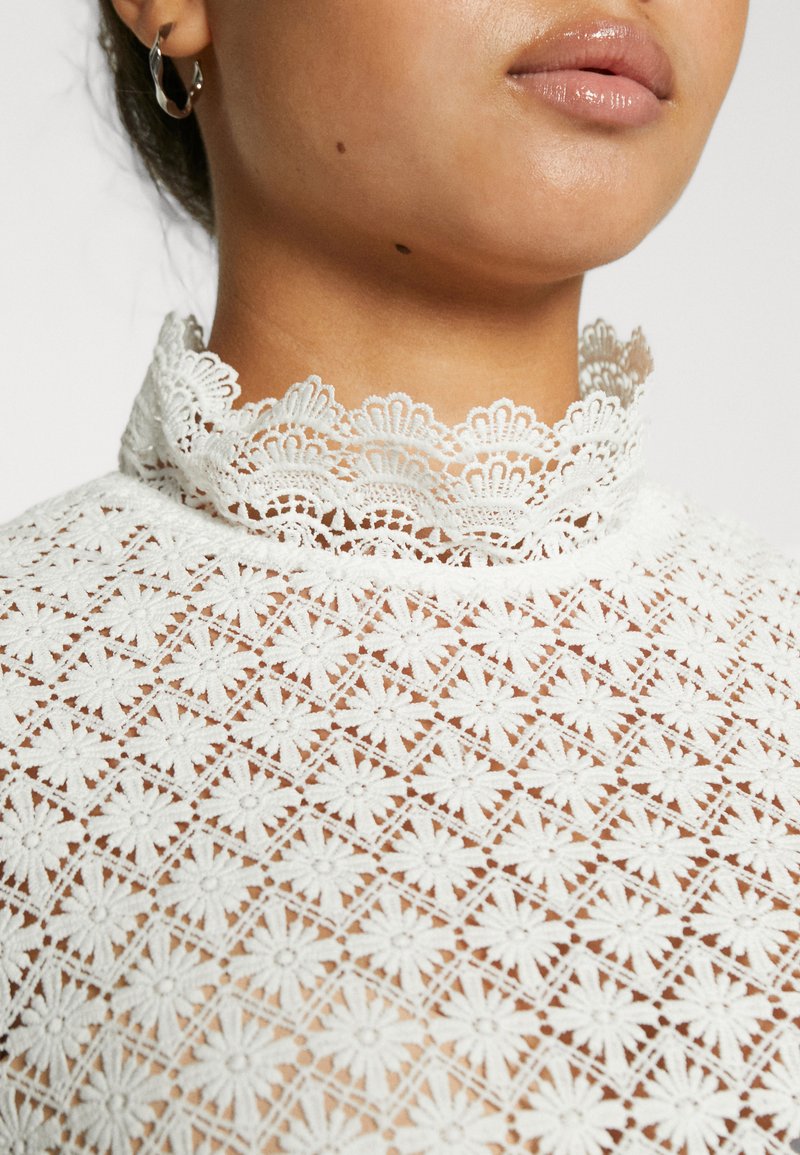 Weißes Spitzentop mit hohem, gewelltem Kragen. Verfügt über florale Muster und eine durchsichtige Textur, die komplizierte Stickereien zeigt.