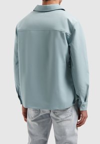 Lichtblauw button-up shirt met een kraag, met een soepele textuur en een pas achter. Gecombineerd met vervaagde lichte jeans.