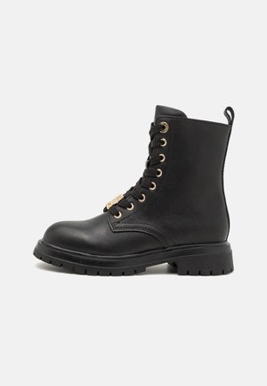 Stivale alla caviglia in pelle nera con punta rotonda, occhielli dorati, lacci neri e suola testurizzata; presenta una linguetta al retro per facilitarne l'indossamento.