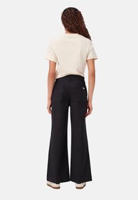 Schwarze weite Jeans aus Denim mit hoher Taille, Gesäßtaschen und glatter Oberfläche, kombiniert mit einem cremefarbenen T-Shirt mit kurzen Ärmeln.