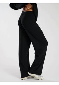 Svarta vida byxor i mjukt tyg med strukturerad yta. Utformade med hög midja och en flödande silhuett, stylade med ljusa sneakers.