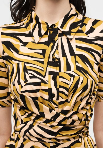 Πουκάμισο με γιακά και κουμπιά, με κοντά μανίκια και αφηρημένο ριγέ μοτίβο σε κίτρινο, μαύρο και μπεζ.