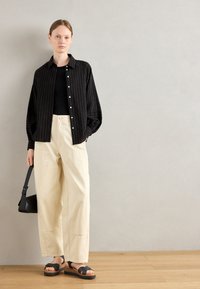 Mustriga musta särk, must peal, kreemivärvi laiad püksid ja mustad platvormsandaalid. Must crossbody-kott täiustab pükse.