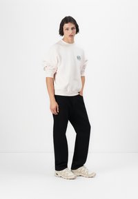 Lichtroze sweatshirt met een ronde halslijn en tekstlogo op de borst, gecombineerd met zwarte broek en beige sneakers. Eenvoudige, relaxte pasvorm.