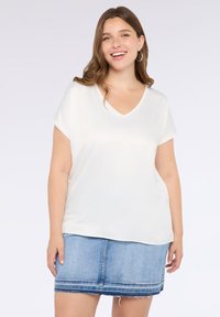 Bluză albă cu decolteu în V și mâneci scurte, fabricată dintr-un material neted, asortată cu o fustă din denim albastru cu margine destrămată și cusături decorative.