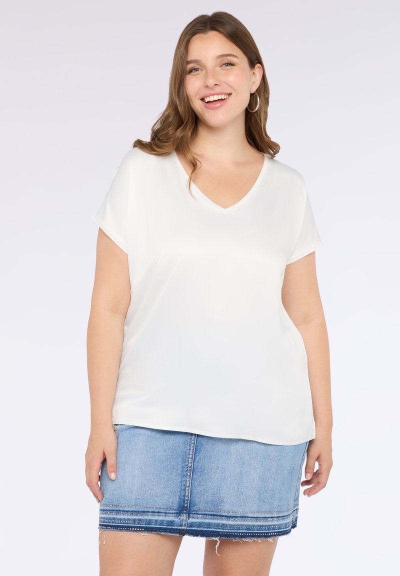 Bluză albă cu decolteu în V și mâneci scurte, fabricată dintr-un material neted, asortată cu o fustă din denim albastru cu margine destrămată și cusături decorative.