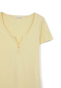T-shirt giallo in cotone a maniche corte con scollo a V e tre bottoni sulla parte anteriore. Tessuto morbido, leggero.