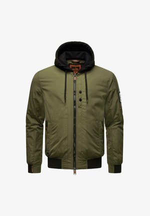 Olive rohelise värvi bomber-jakk, millel on tõmblukk ees, must kapuutsiga särk, soonikud mansettides ja hellel, ning kaks külgtaskut. Vasakul käel on patš.