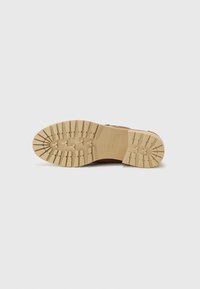 Bottines en cuir brun avec une épaisse semelle en caoutchouc beige texturée présentant des sculptures profondes pour l'adhérence. Accentuées par des coutures le long des bords.