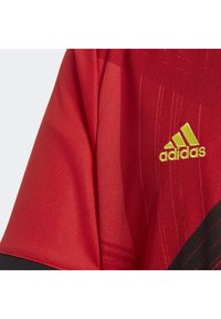 Maglia sportiva rossa con trama in rete traspirante. Presenta il logo Adidas in verde neon, accenti neri e strisce orizzontali dinamiche.