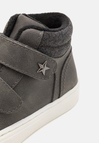 Grauer High-Top-Schuh aus synthetischem Material mit einem strukturierten Wollkragen, Klettverschlussriemen und einem silbernen Sternakzent auf dem Riemen.