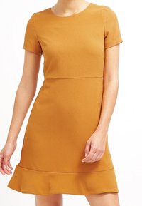 Senapsgul kortärmad klänning med figurnära liv, utsvängd fåll, textil med struktur och sömdetaljer vid midjan.