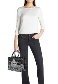 Borsa tote in pelle nera con design grafico e logo "BRACCIALINI", abbinata a una maglia bianca a maniche lunghe e jeans scuri in denim.