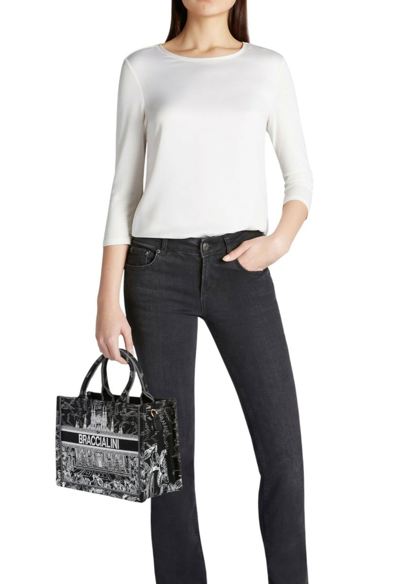 Borsa tote in pelle nera con design grafico e logo "BRACCIALINI", abbinata a una maglia bianca a maniche lunghe e jeans scuri in denim.
