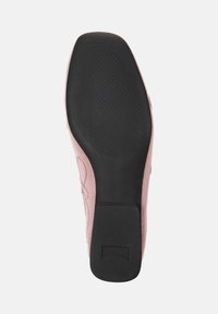 Sula av skon med en texturerad svart gummibotten och ett slätt rosa tyg på ovansidan, rundad form och en liten klack.