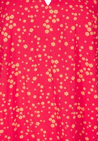 Tela roja con un patrón floral que presenta pequeñas flores beige. El diseño es ligero, con escote en V y una textura suave.