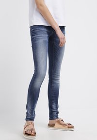 Slim-fitting, urtvättade blå denimjeans med en mjuk textur. Bärs med ljusbruna sandaler med metalliska detaljer och en kraftig sula.