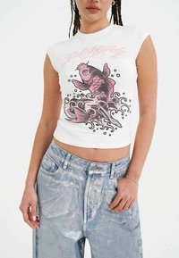 White fitted t-shirt with pink fish graphic and wave design. Short sleeves and a crew neck. Paired with light blue distressed jeans.