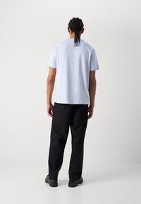 Ljusblå kortärmad t-shirt med avslappnad passform, kombinerad med svarta vida byxor och svarta skor. Minimalistisk design, inga synliga mönster.