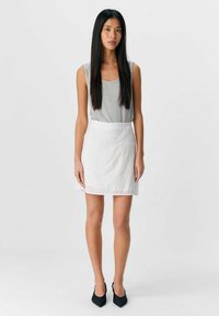 Top gris sin mangas combinado con una mini falda blanca bordada. El conjunto presenta un diseño ajustado y se complementa con zapatos de punta negra.