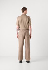 T-shirt polo beige à manches courtes, associé à un pantalon loose léger marron clair avec une taille élastique et deux poches arrière.