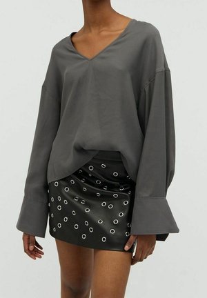 Losse grijze V-hals top met lange mouwen, gecombineerd met een zwarte minirok met zilveren oogjesdetails op de stof.