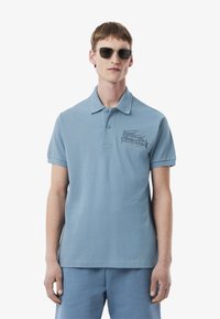 Jasnoniebieska koszulka polo wykonana z bawełny o miękkiej teksturze, z trzema guzikami przy kołnierzyku oraz haftowanym logo po lewej stronie klatki piersiowej.