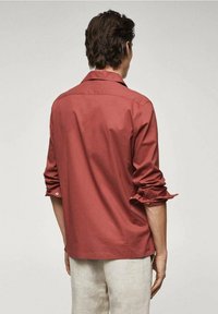 Rood katoenen overhemd met een ontspannen pasvorm, lange mouwen opgerold bij de manchetten, een enkele knoop aan elke mouw en een klassieke kraag.