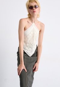 Háčkovaný top na krk v off-white farbe s vlnitými okrajmi a geometrickými vzormi, skombinovaný s tmavošedou, priliehavou suknou.