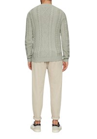 Pullover in Hellgrün mit einem Kabelstrickdesign, runder Ausschnitt und gerippten Bündchen. Kombiniert mit hellbeigen Hosen und Sneakers.