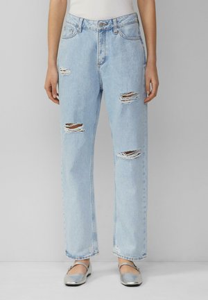 Jean en denim bleu clair avec une coupe ample, présentant plusieurs déchirures aux genoux, une taille haute et un design classique à cinq poches. Fermeture à bouton argenté.