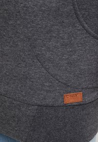 Szary sweter z teksturowanej tkaniny, z przednią kieszenią oraz brązową skórzaną metką z nazwą marki na dolnej części.